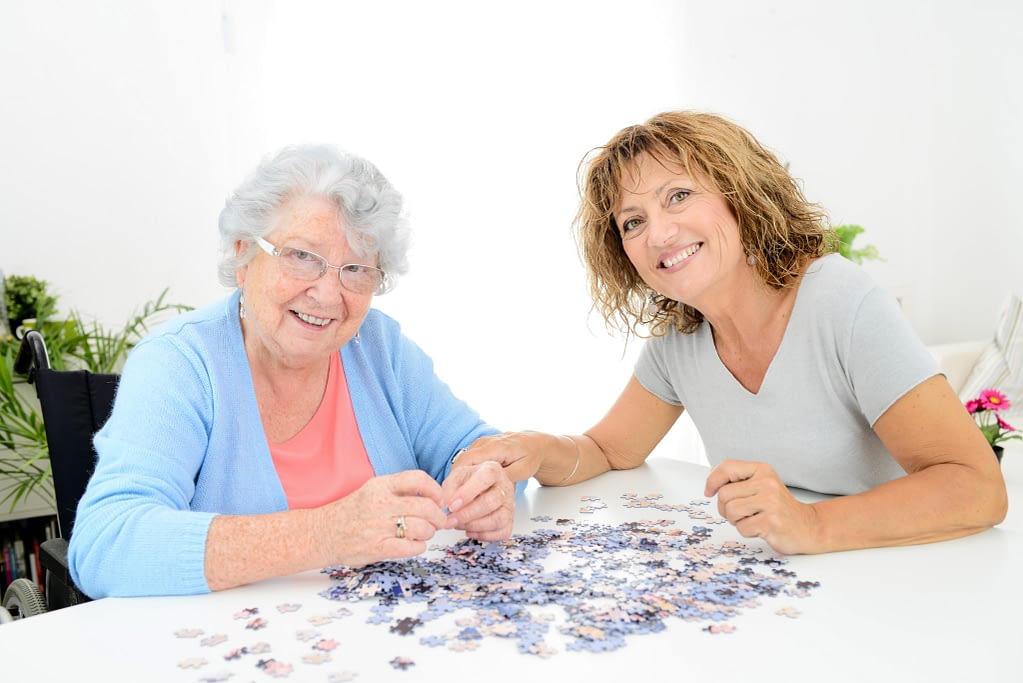 cheerful mature woman doing puzzle and spending time with elderly senior woman at home
