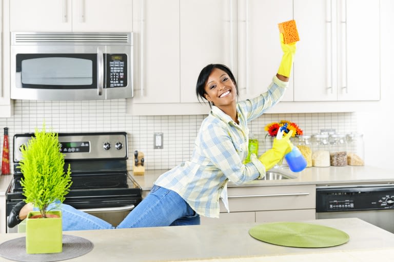 Smiling young black woman dancing and enjoying cleaning kitchen